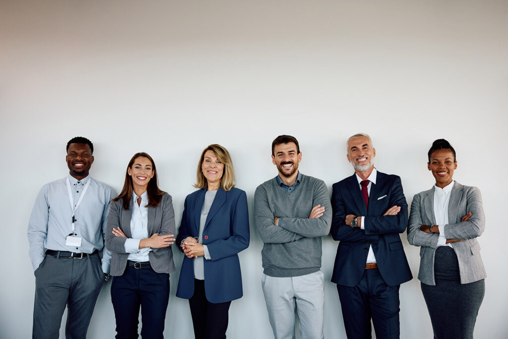Mixed age group of happy business colleagues against wall looking at camera.